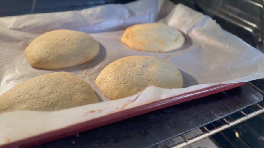 Four baked New York Black and White cookies on parchment paper in a baking pan, golden brown on bottom.