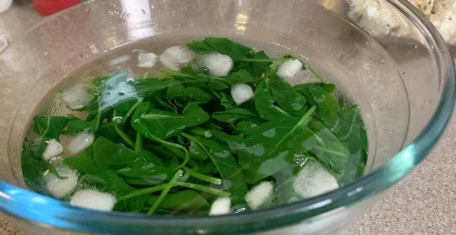 Fresh spinach in ice water bath for blanching in a glass bowl.