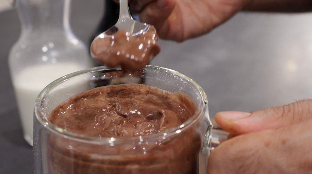 Spooning rich chocolate sauce into a glass jar of creamy chocolate spread or mousse.