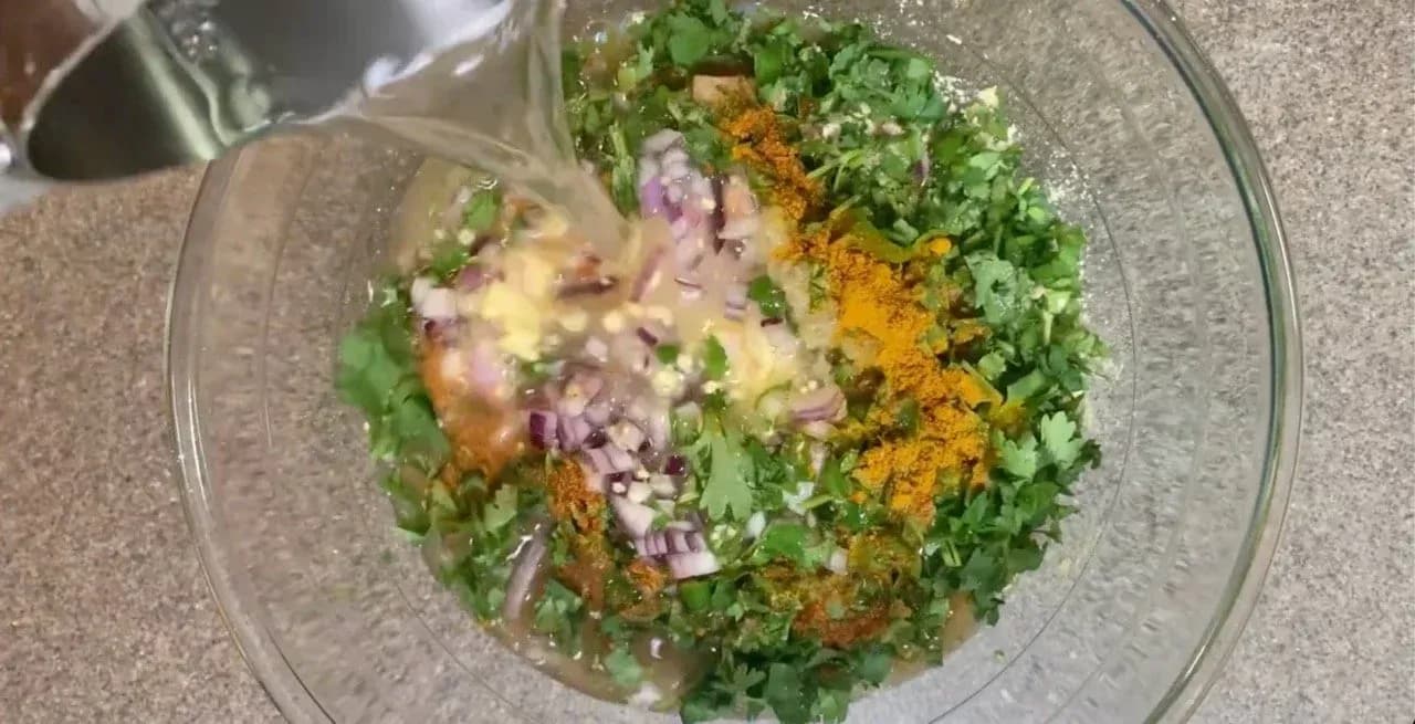 Besan chilla batter in glass bowl with chopped onions, cilantro, and turmeric mixed together before cooking.