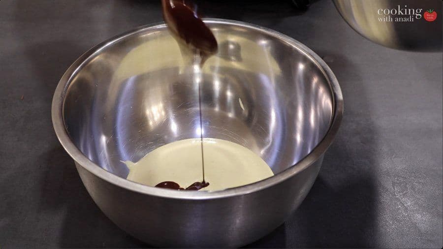 Pouring dark chocolate mixture into a bowl of whipped egg whites for folding.