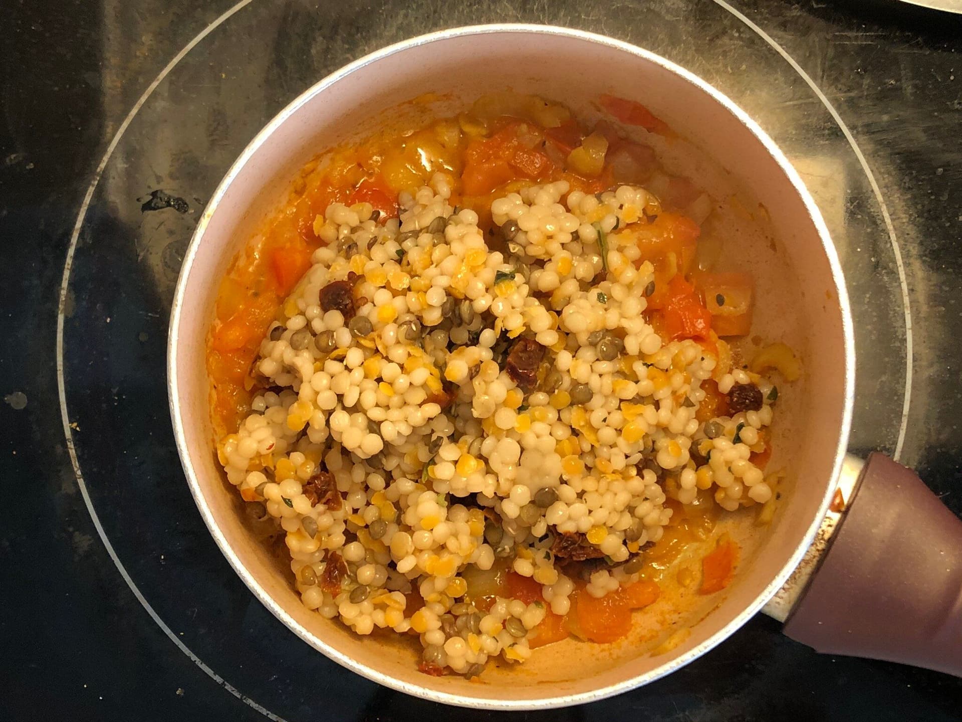 Couscous being added to a simmering tomato-based sauce in a pot with visible spices and ingredients.