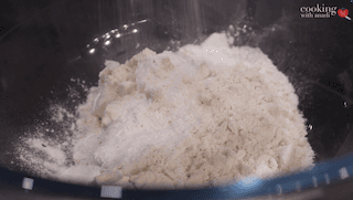 Dry ingredients for sugar cookie waffles mixed in a dark bowl: flour, baking powder, salt, and cinnamon.