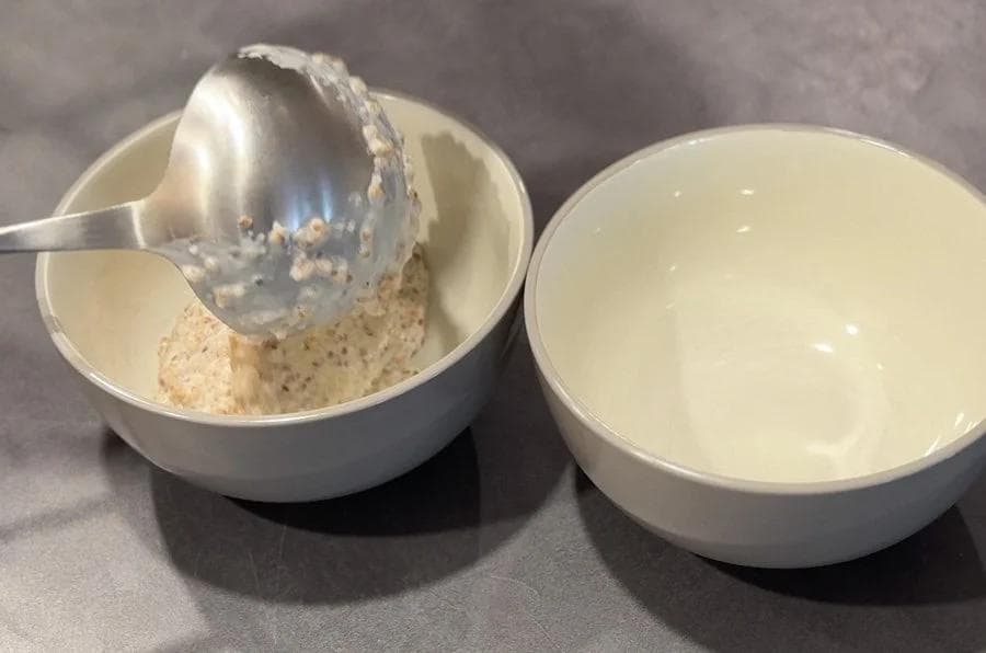 Roasted cracked wheat in a white bowl with a spoon, beside a bowl of milk for Instant Pot Meetha Dalia.