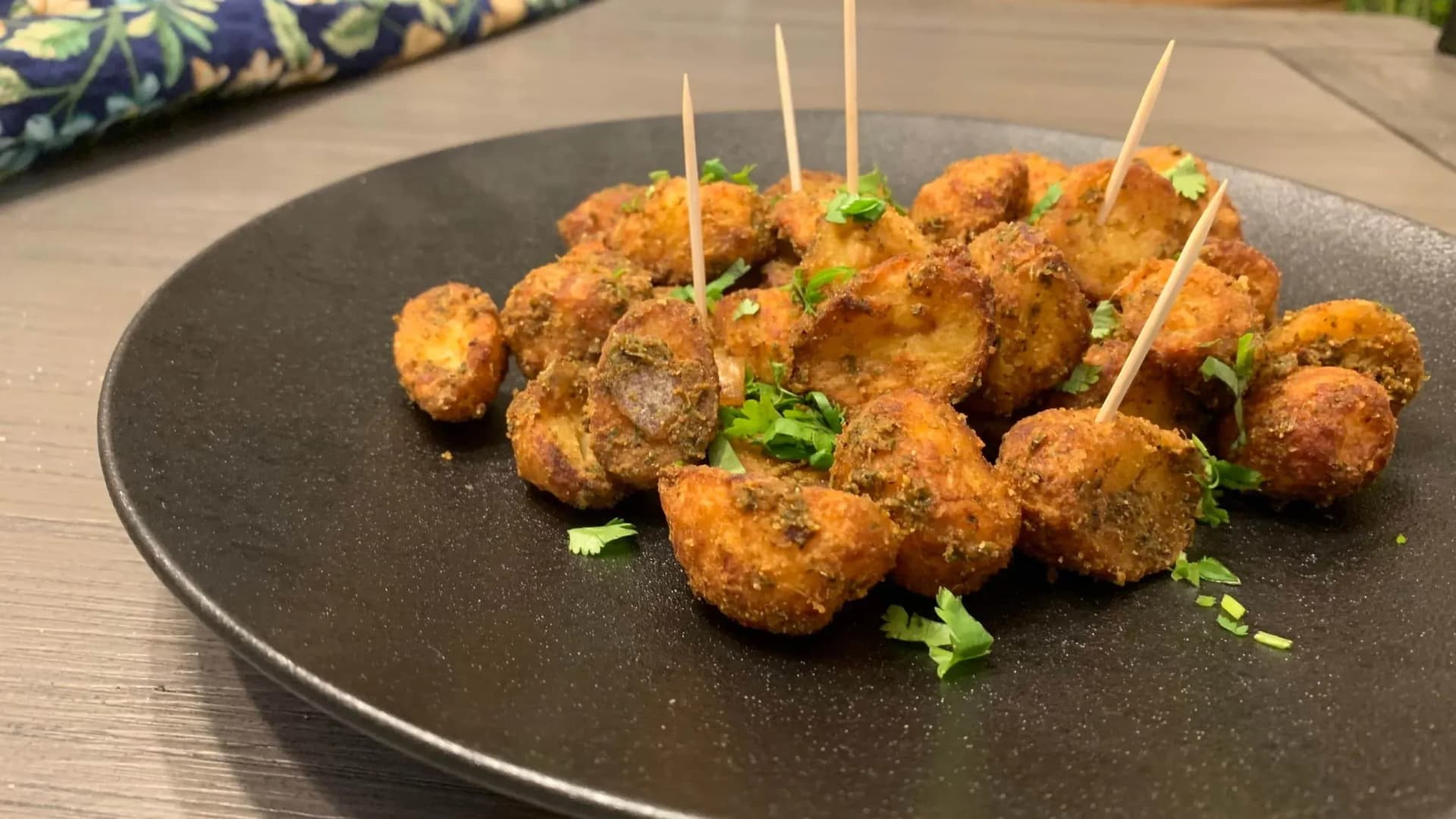 Golden air-fried baby potatoes garnished with fresh cilantro and toothpicks on a dark plate.