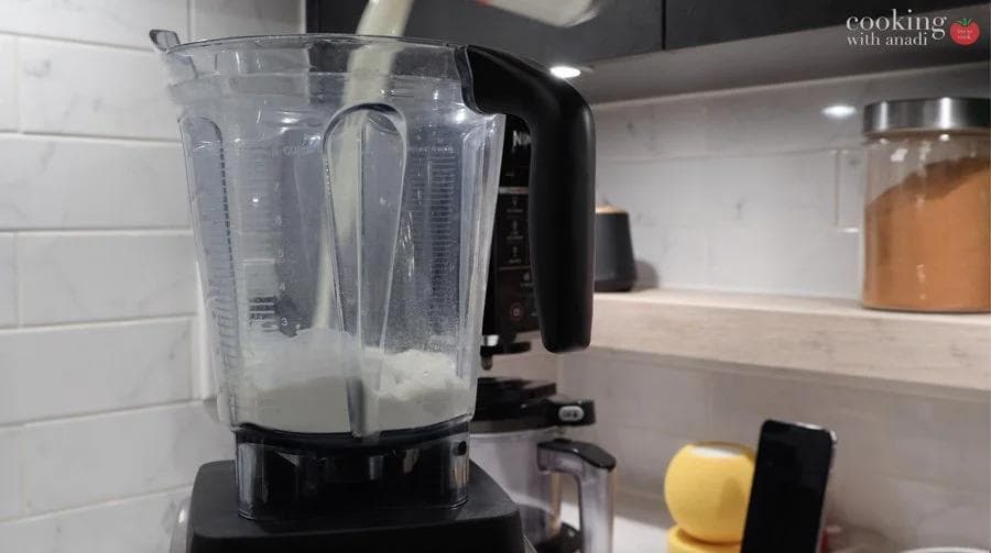 Blender filled with crepe batter ingredients on kitchen counter next to a yellow apple.