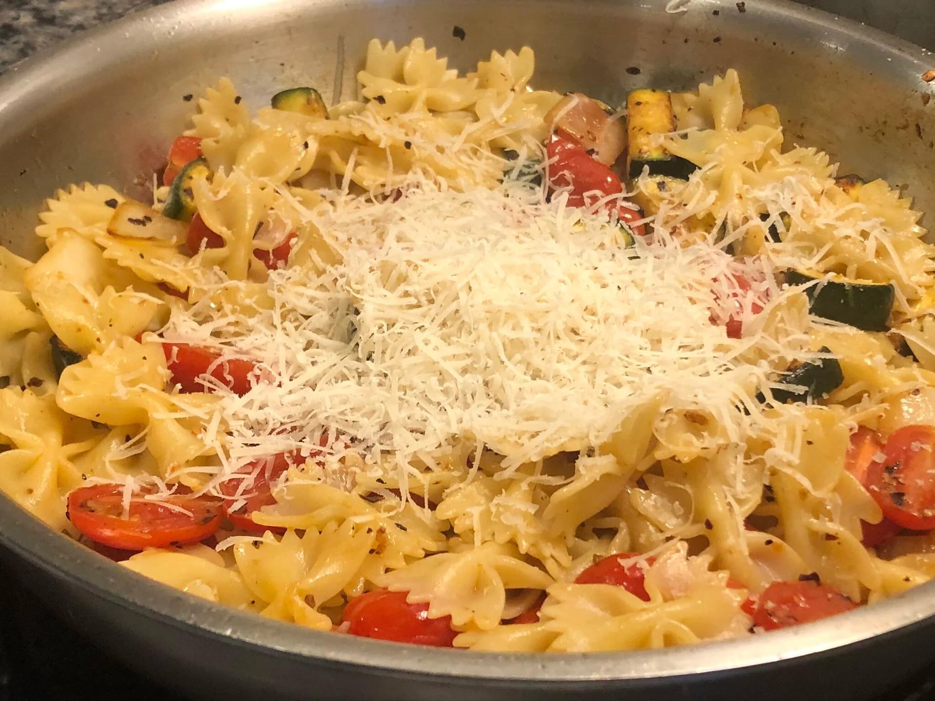 Bow-tie pasta with red peppers and zucchini topped with grated Parmesan cheese in a skillet.