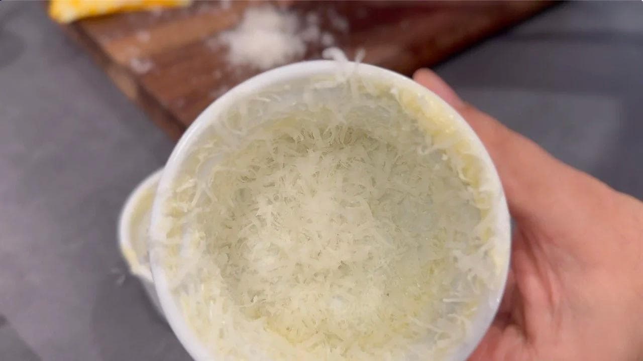 A white ramekin coated with melted butter and grated Parmesan cheese on the interior walls.