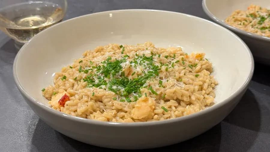 Creamy lobster risotto garnished with fresh green chives in a white bowl, served with white wine.