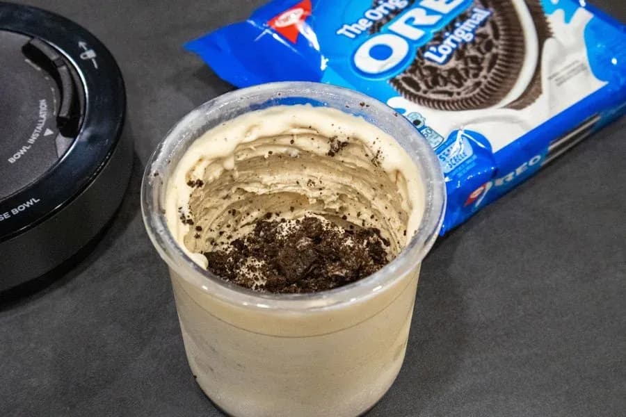 Homemade high-protein Oreo ice cream mixture in a container with crushed cookie pieces on top, next to an Oreos package.