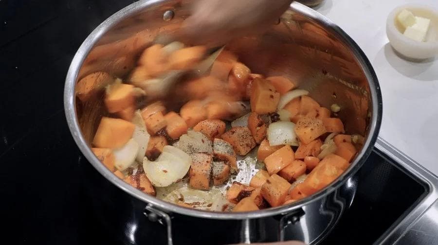 Pot of diced carrots, onions, and seasoned ground meat simmering in broth on stovetop.