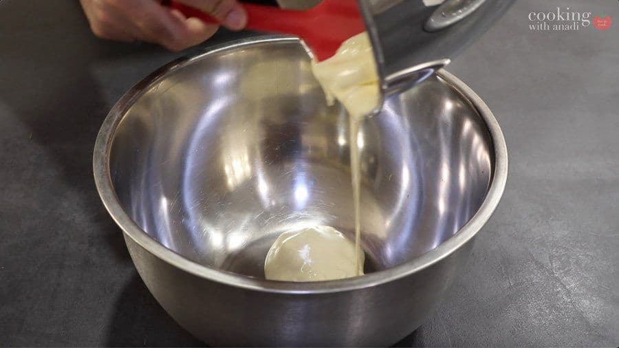 Pale, thick egg yolk mixture at ribbon stage being poured into a stainless steel mixing bowl.