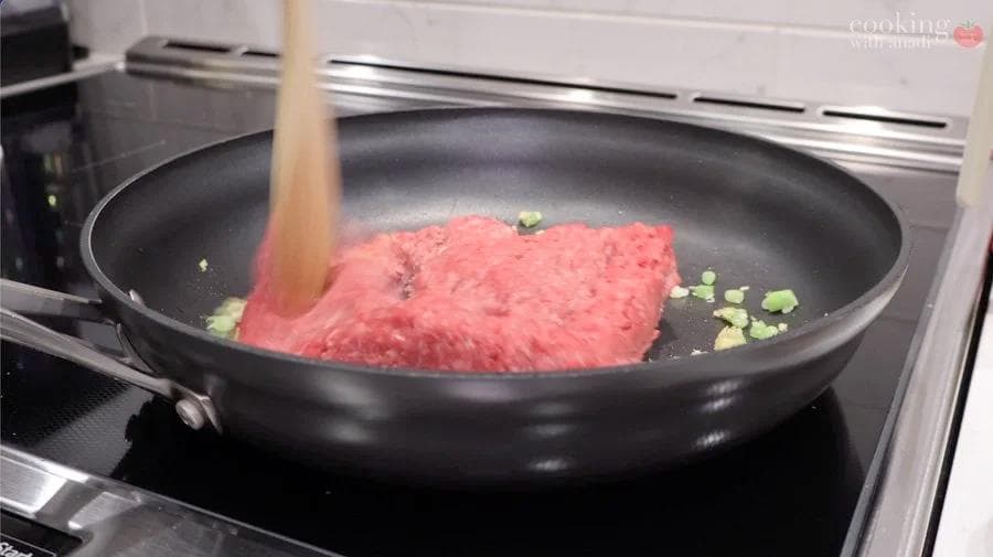 Ground beef being browned in a skillet with garlic and green onions for egg roll in a bowl.