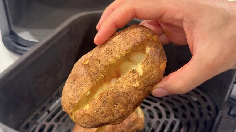 Hand holding a crispy-skinned potato shell with fluffy interior visible, demonstrating the scooped potato for twice baked preparation.