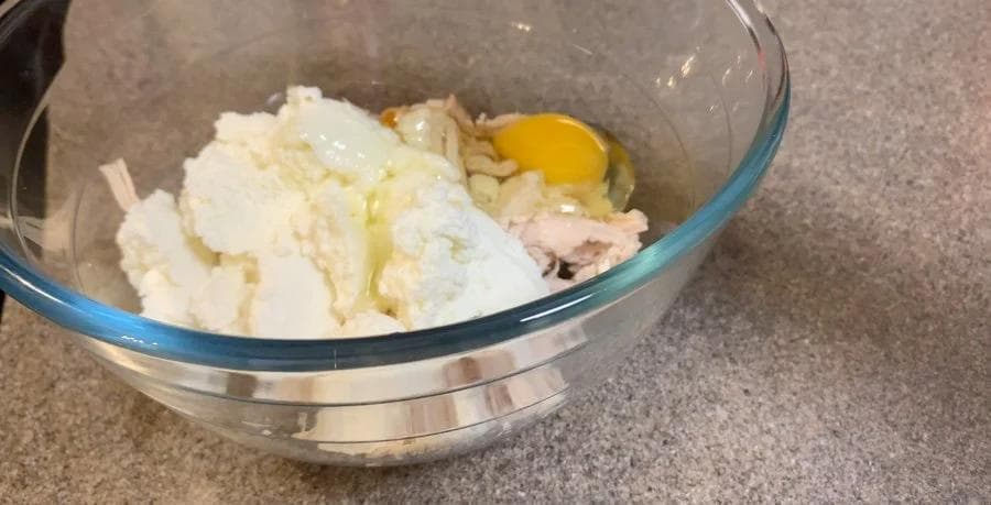Ricotta, egg, and ground chicken mixed together in a glass bowl for lasagna filling.