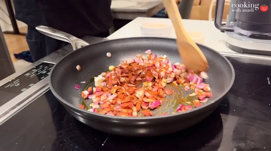 Diced red onions and carrots sautéing with paprika in a nonstick skillet, stirred with a wooden spatula.