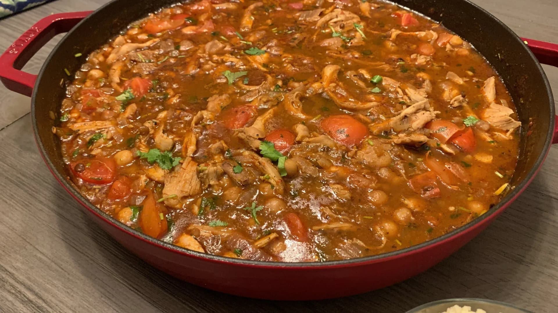 One-pot Moroccan chicken and chickpea stew with tomatoes and fresh parsley in a red Dutch oven.