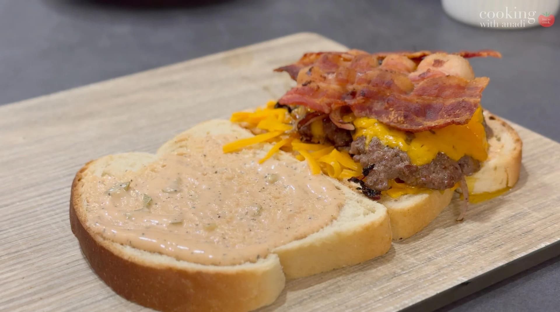 Smash burger patty melt with melted cheddar cheese, crispy bacon, and caramelized onions on toasted bread with sauce.