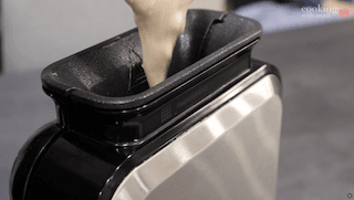 Batter being poured into a preheated waffle maker with black interior and white exterior.