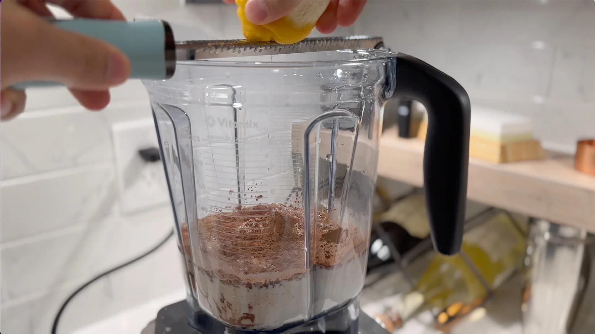 Pouring yellow liquid into a food processor containing chocolate crepe batter mixture