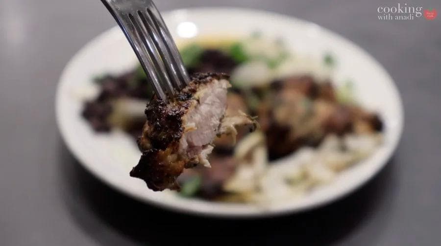 Fork lifting a piece of moist, browned mojo chicken above a white plate with sides