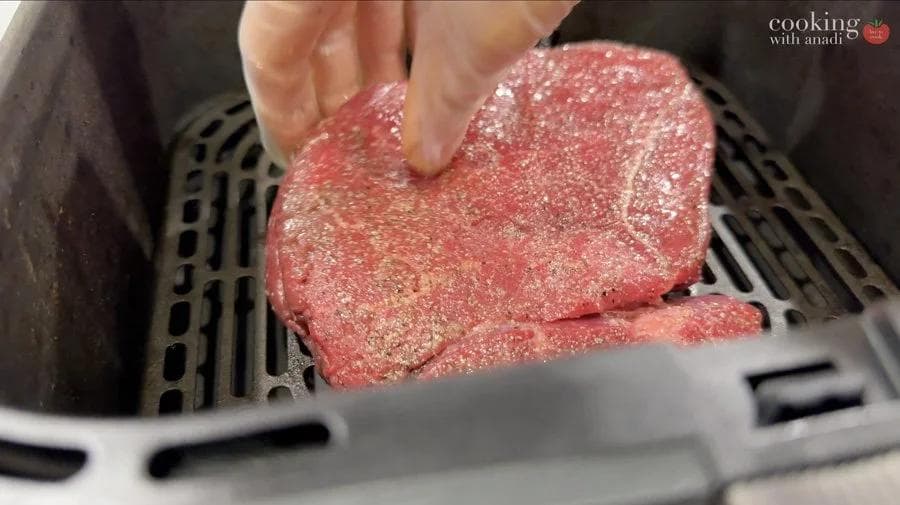Seasoned raw sirloin steak being placed in air fryer basket for cooking.