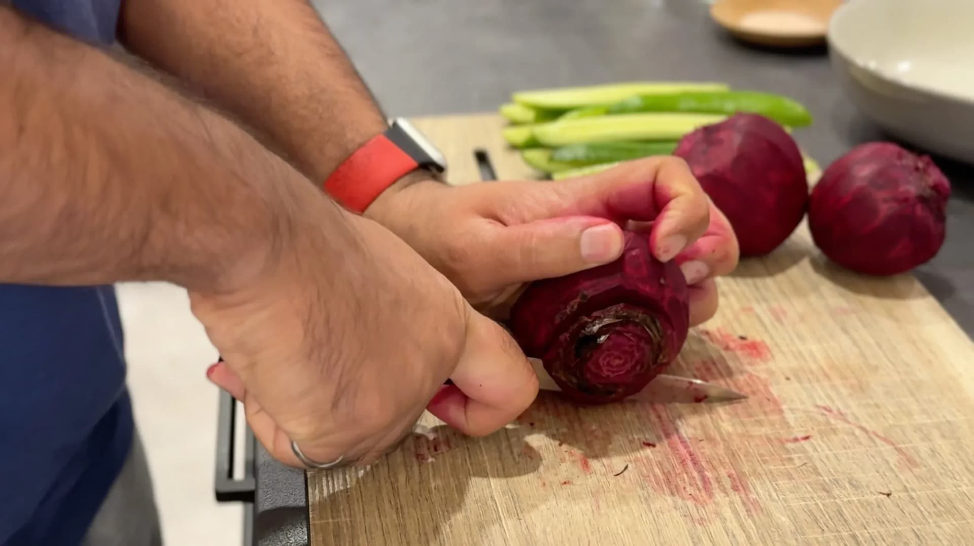 Hands peeling a raw beet on a wooden cutting board with green beans and other beets nearby.