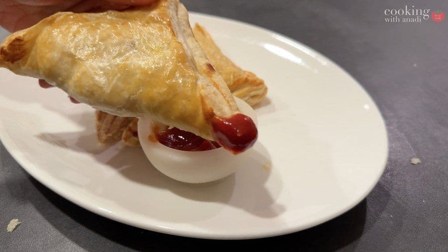 Golden baked potato puff pastry with sliced hard-boiled egg and red chili on a white plate.