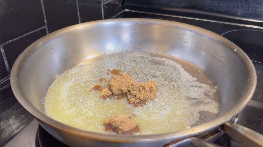 Melted butter, brown sugar, and cream mixture simmering in a pan with apple pie spice sprinkled on top.