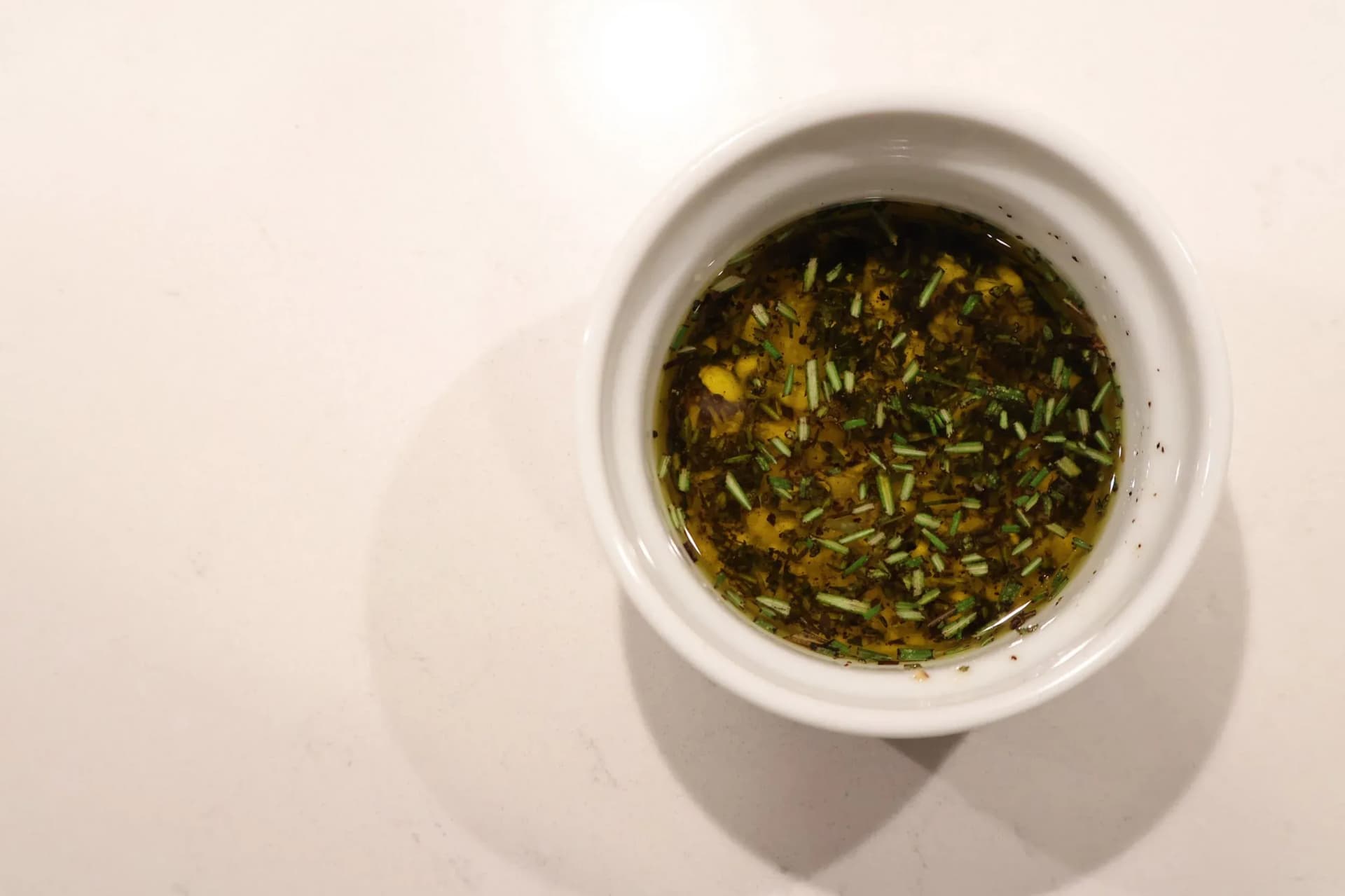 Small white ramekin filled with olive oil, minced garlic, and chopped fresh rosemary and herbs