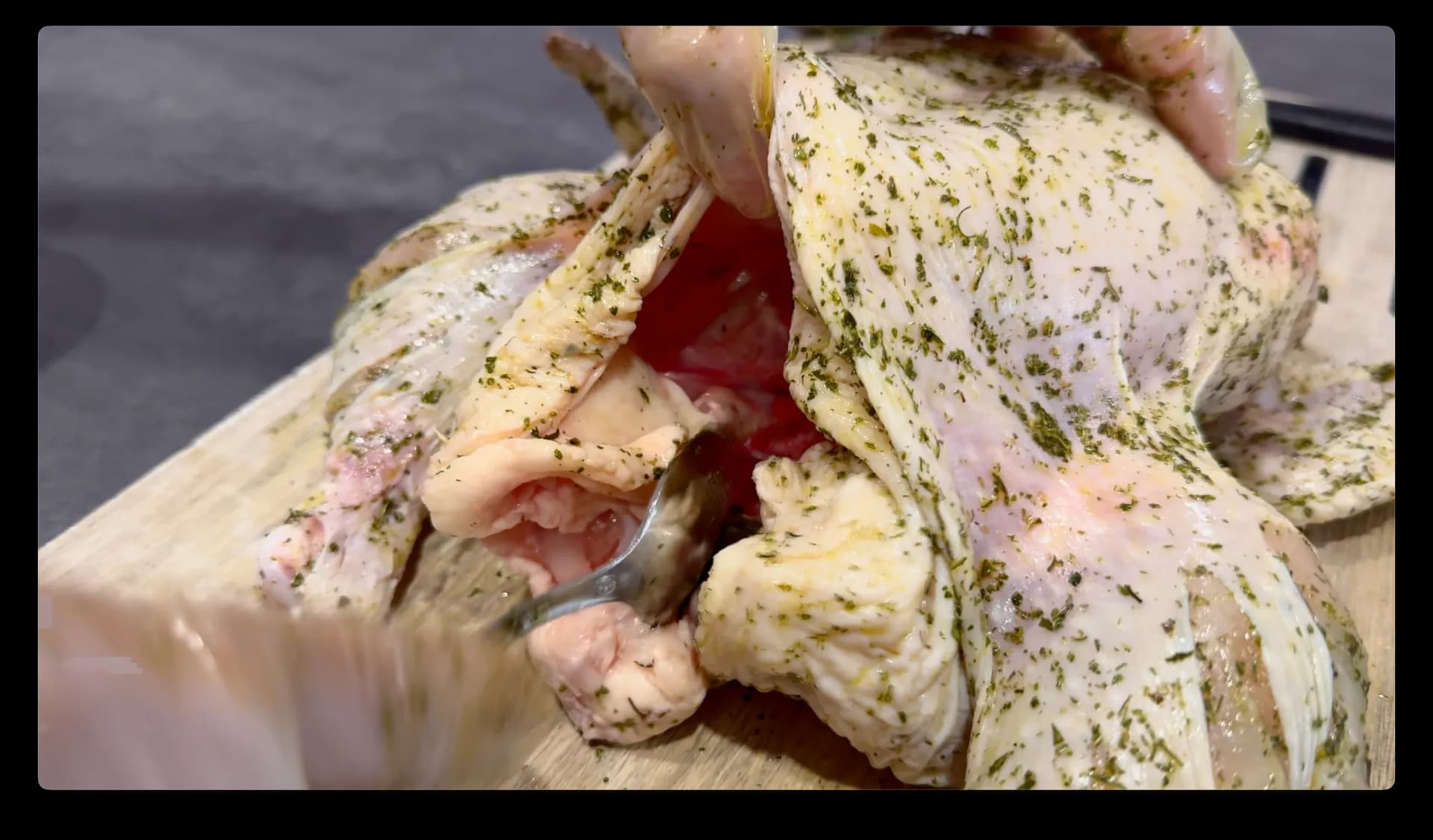 Herb and lemon paste being rubbed over a raw whole chicken on a wooden cutting board.