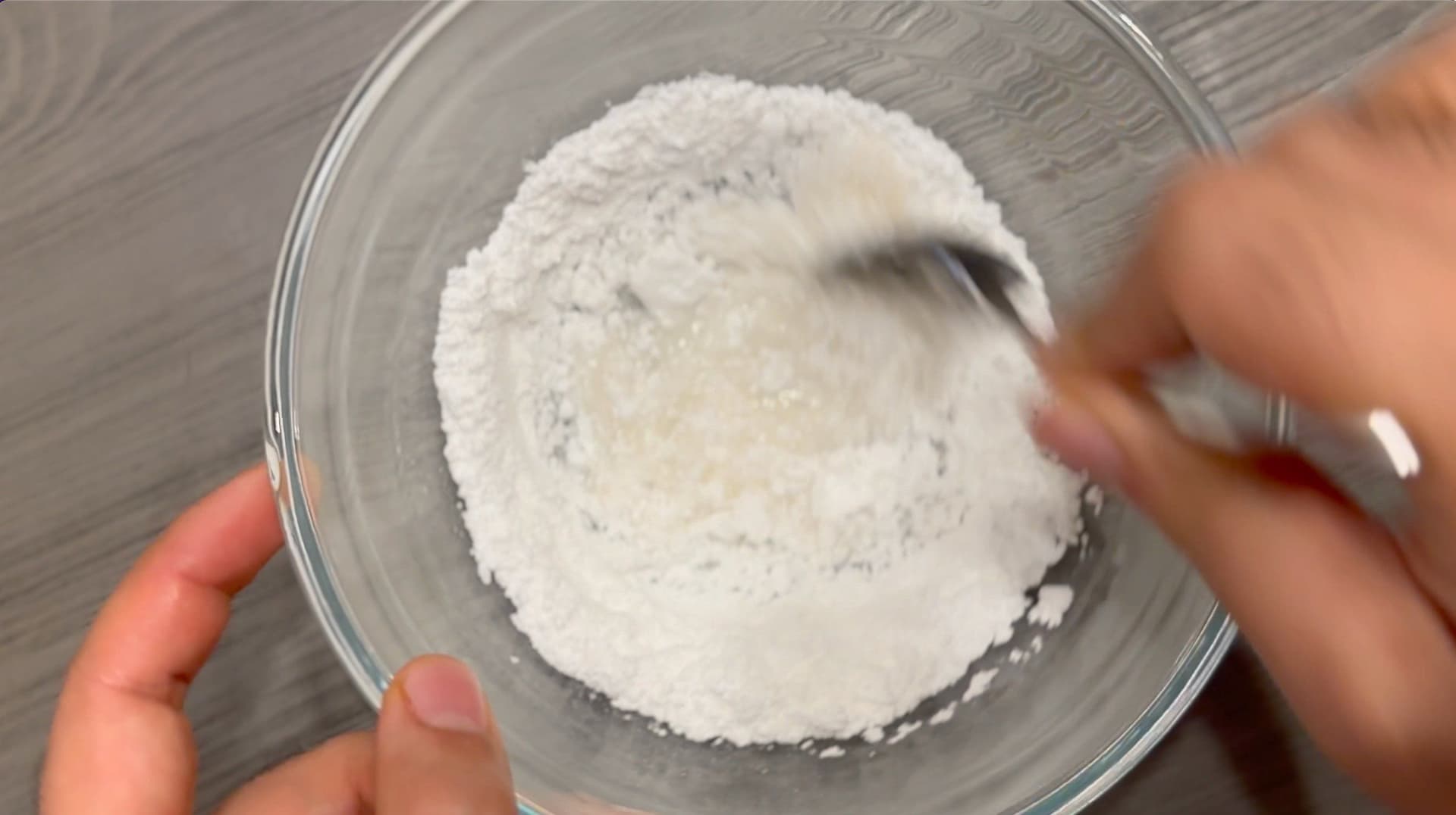 Whisking together confectioners sugar and liquid ingredients in a glass bowl for cinnamon roll icing.