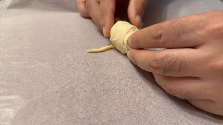 Hands wrapping crescent roll dough around a cocktail sausage to form a pig in a blanket.