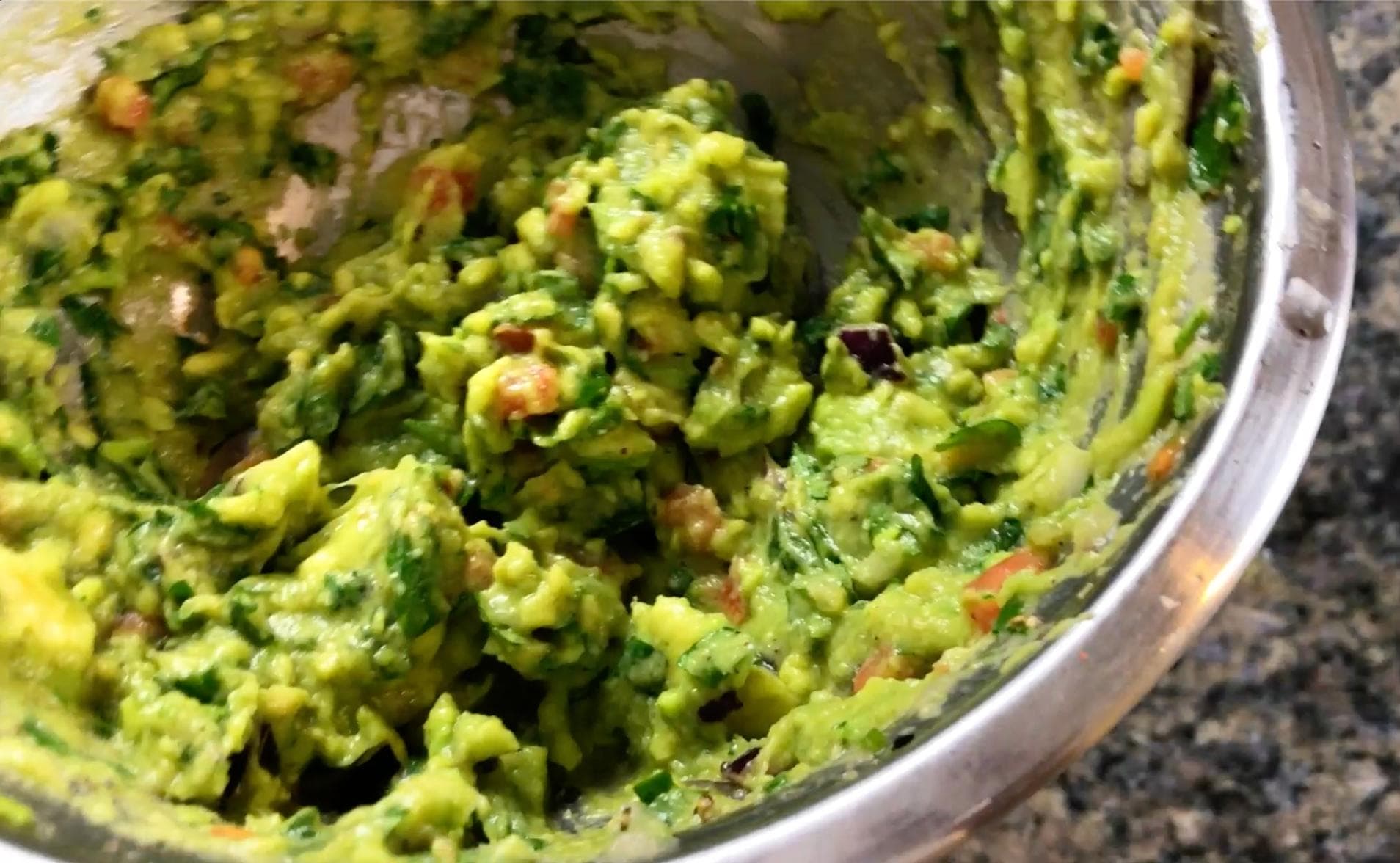 Freshly prepared guacamole in a bowl showing mashed avocado mixed with diced tomatoes, onions, cilantro, and green chilies.