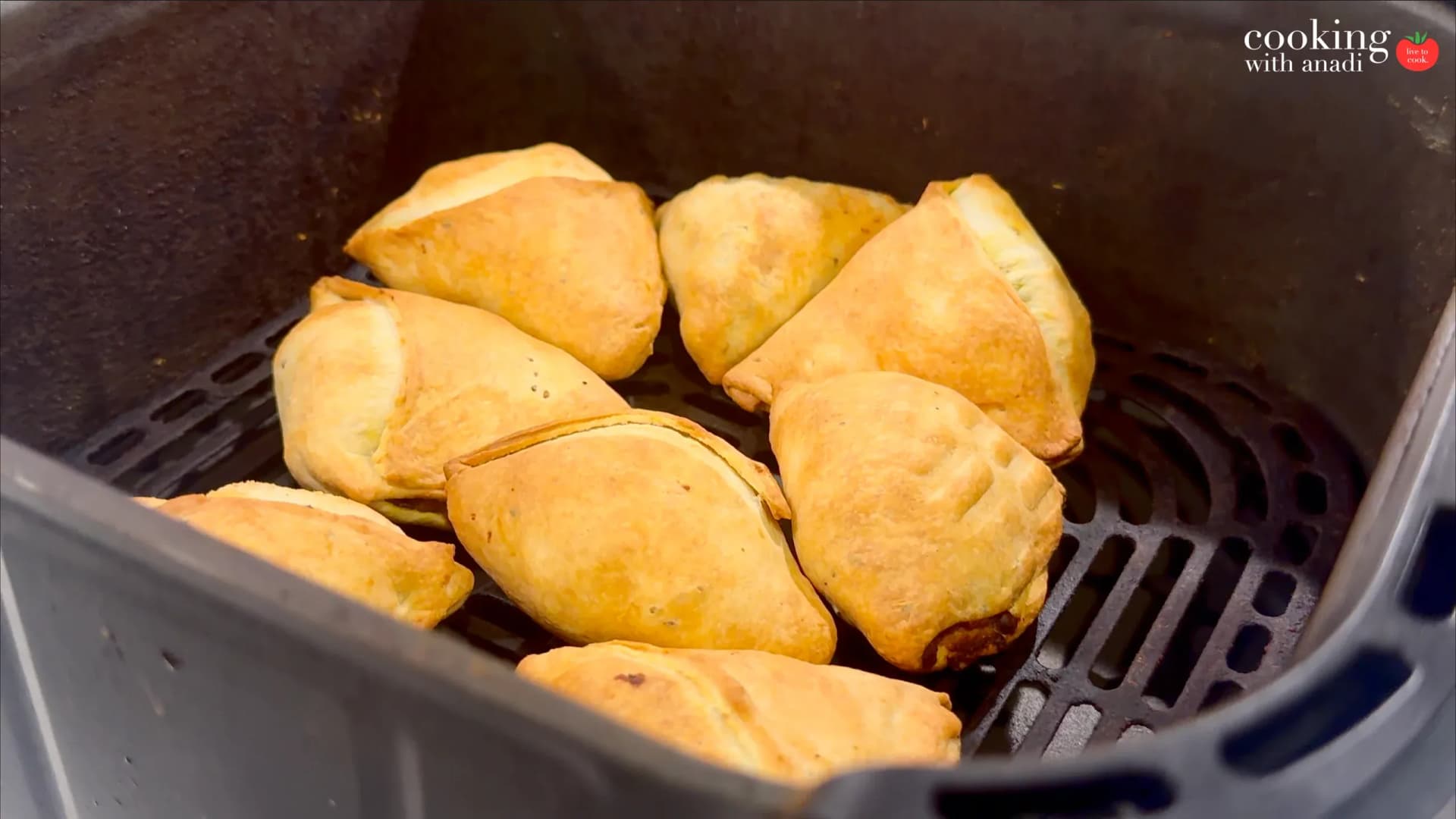 Golden brown crispy samosas in an air fryer basket during cooking.