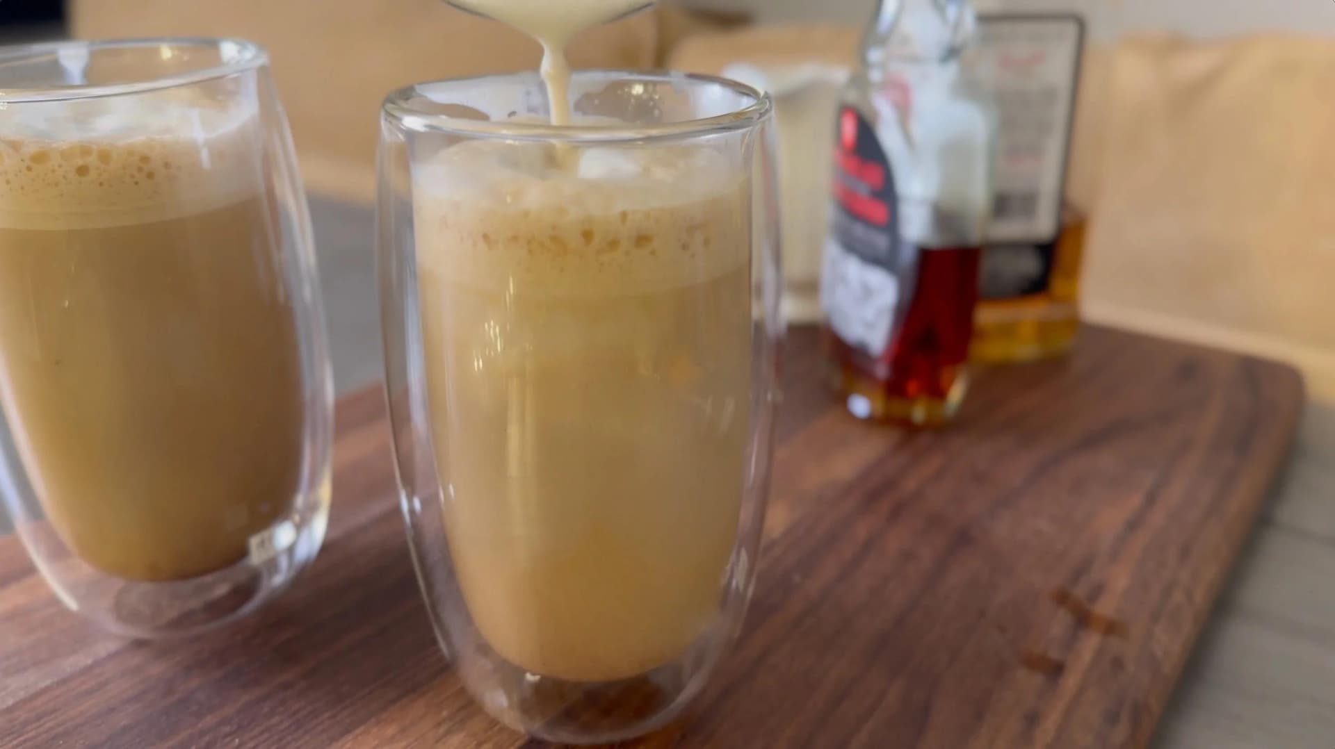 Two double-walled glasses filled with maple bourbon latte on a wooden board, ready to serve.