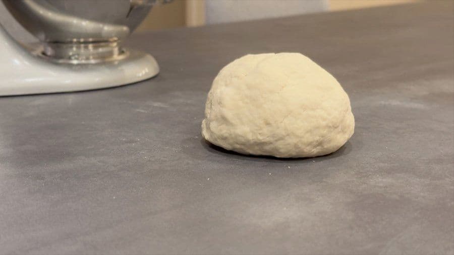 A ball of white pizza dough on a gray countertop next to a stand mixer.
