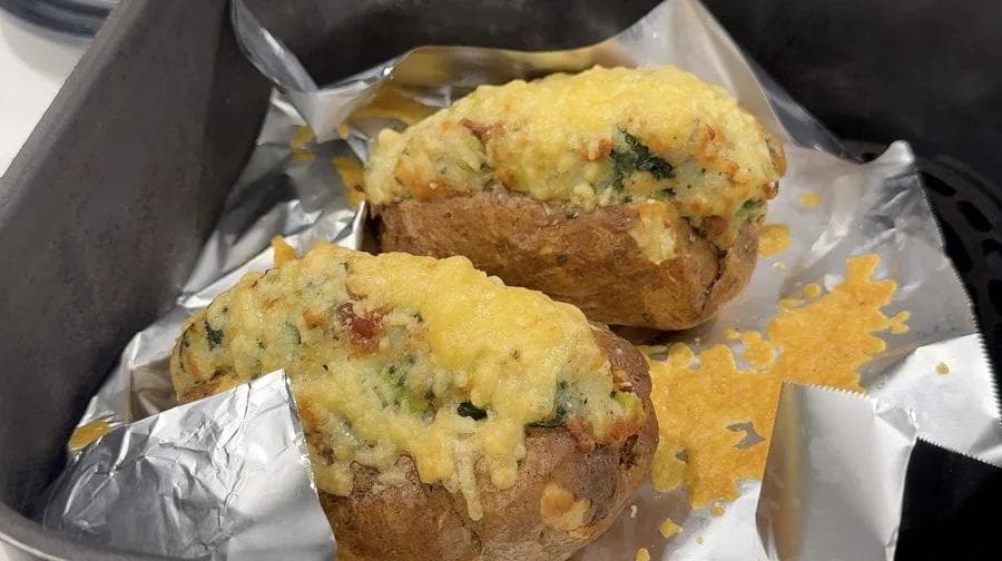 Two air fryer twice baked potatoes with melted golden cheese and herb filling on parchment paper.