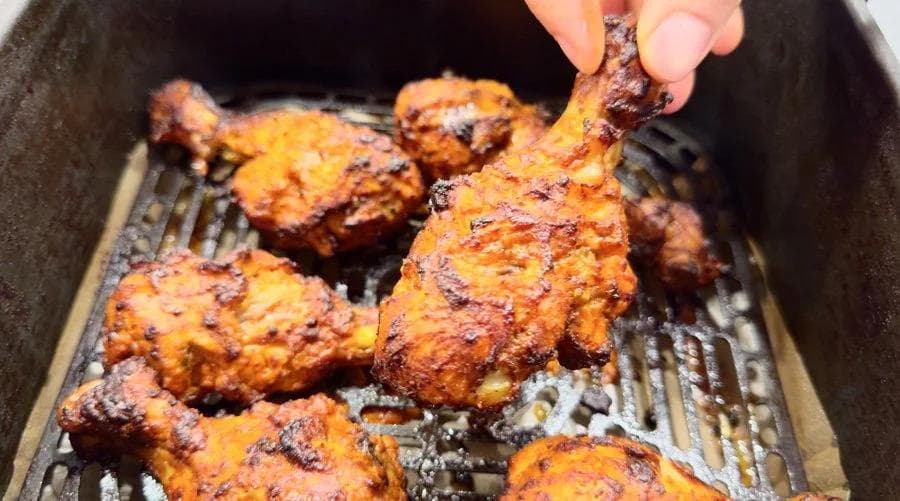 Crispy golden-brown tandoori chicken pieces in an air fryer basket being brushed with butter.