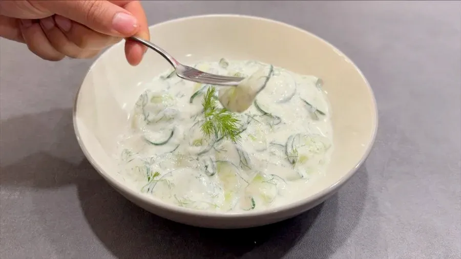 Creamy German cucumber salad garnished with fresh dill in a white bowl with a spoon.