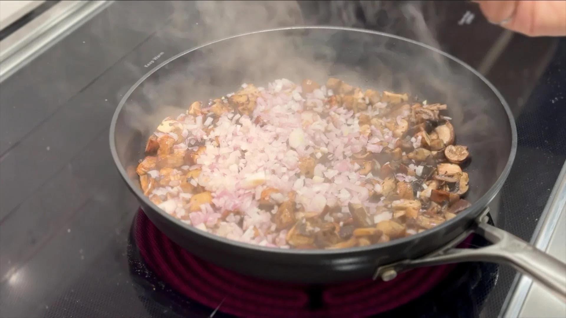 Sautéed mushrooms and diced shallots cooking in a pan with steam rising from the mixture.