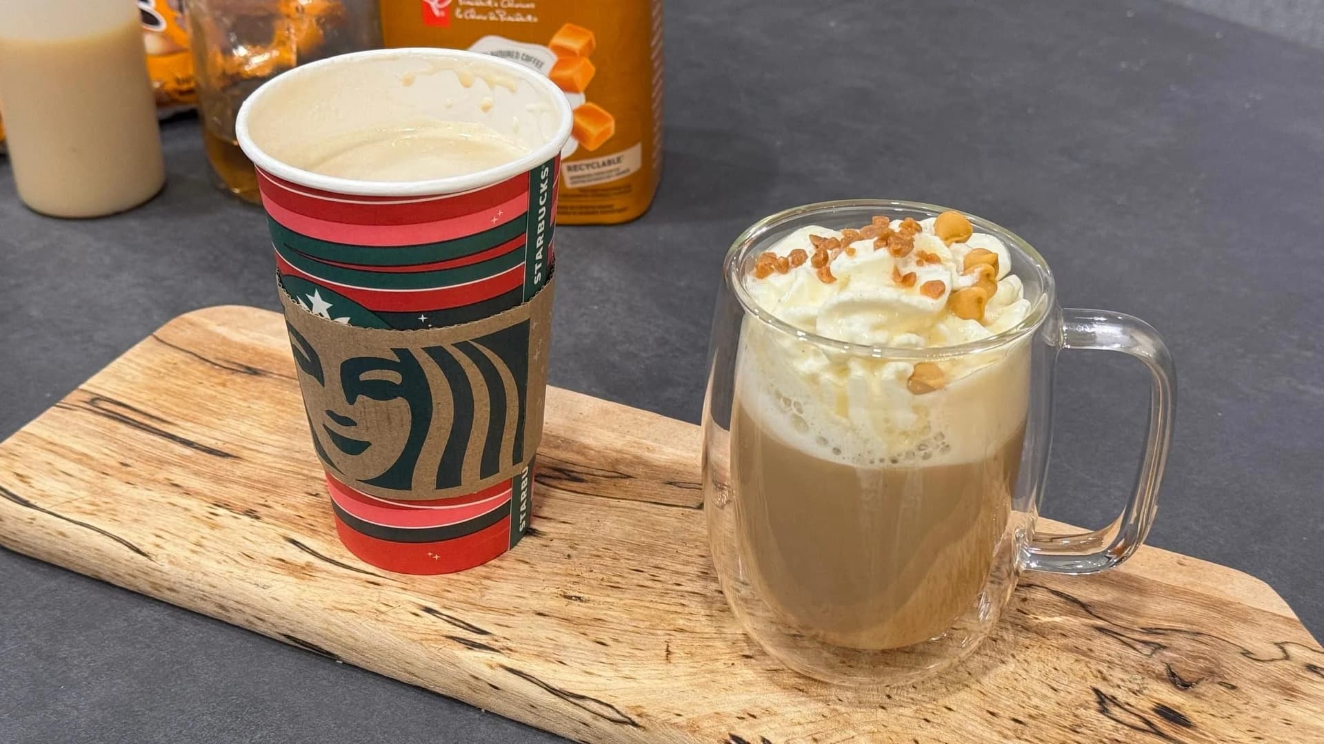 Homemade Caramel Brulee Latte topped with whipped cream, caramel drizzle, butterscotch chips, and toffee bits in a glass mug and Starbucks cup.