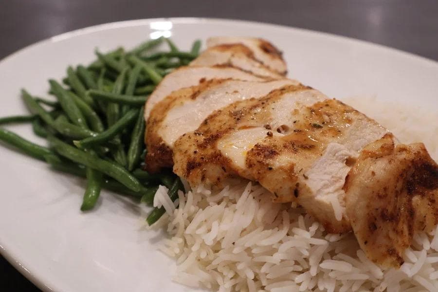 Sliced air fryer chicken breast served over white rice with fresh green beans on a white plate