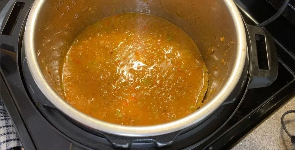 Instant Pot with arroz con pollo ingredients mixed together before pressure cooking, showing golden broth with rice and chicken.