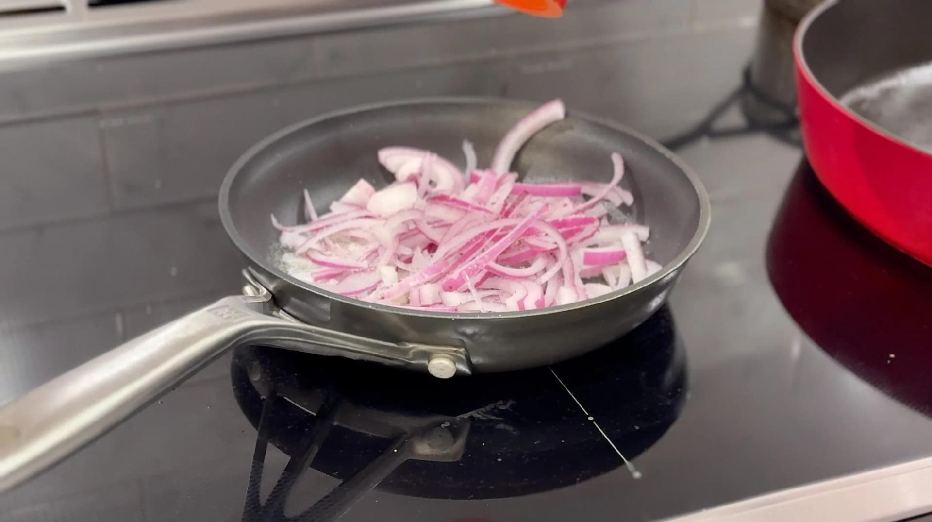Sliced pink onions cooking in butter in a skillet on a stovetop burner.