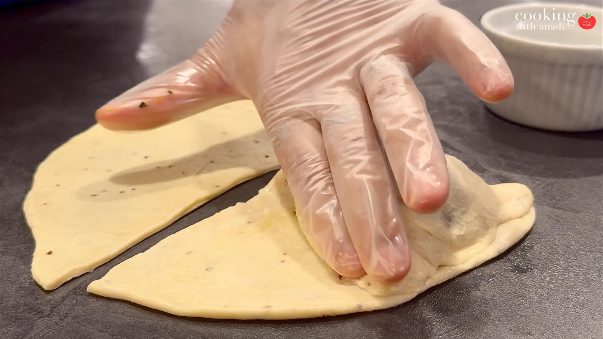 Hands in plastic gloves folding a samosa pastry in half and sealing the edges to form a triangle shape.