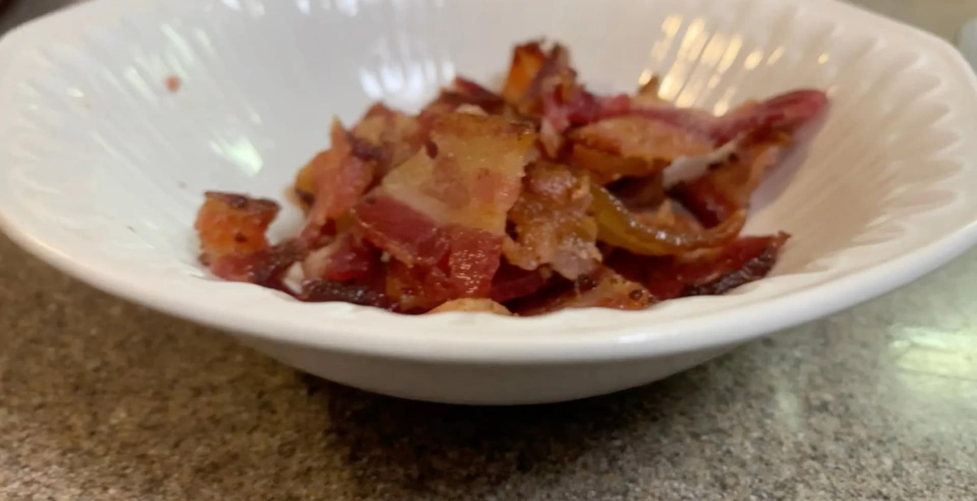 Chopped crispy bacon pieces in a white bowl, ready to be added to poutine.