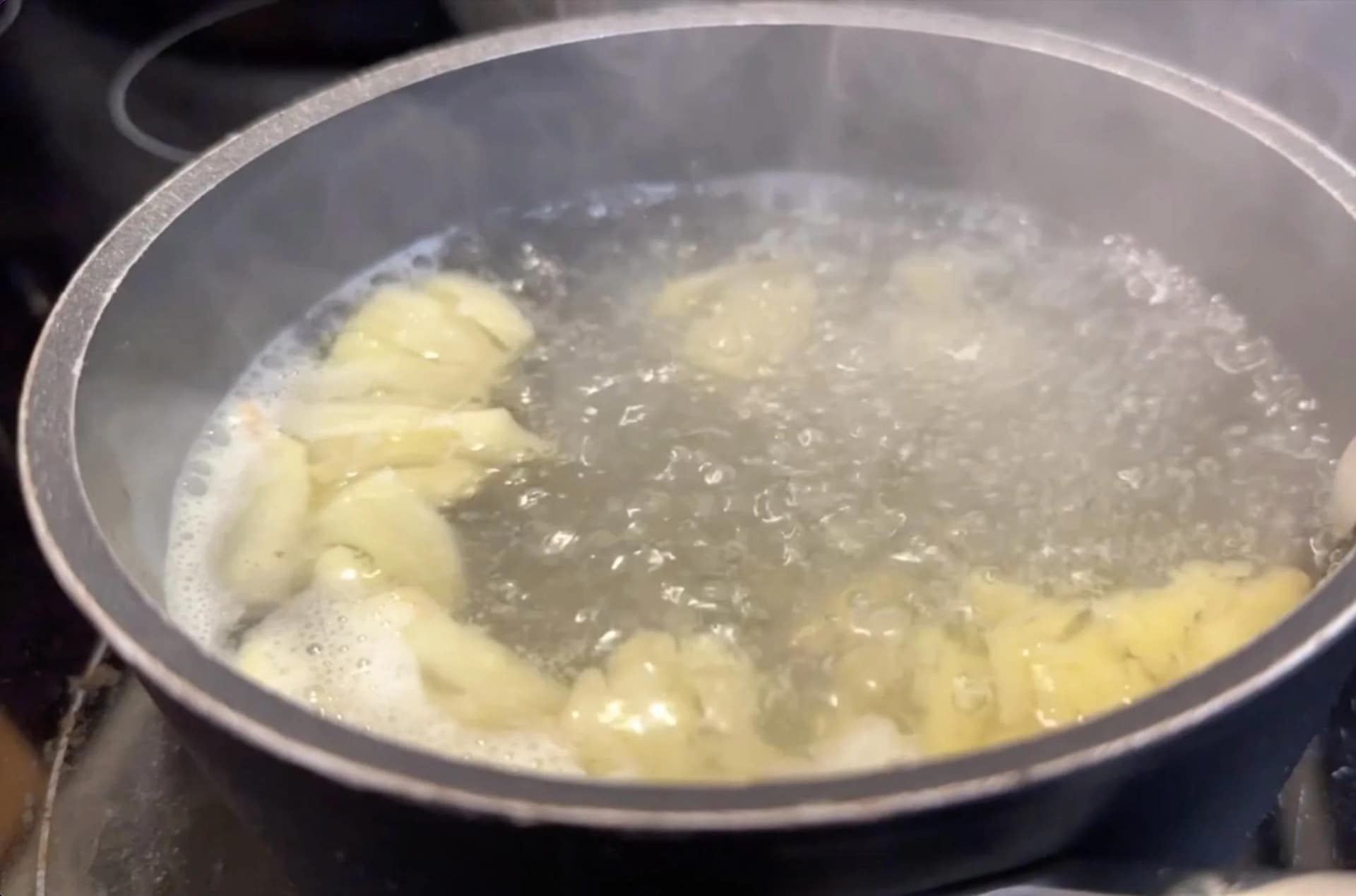 Boiling ginger pieces in water in a saucepan, water turning yellow from the ginger infusion.