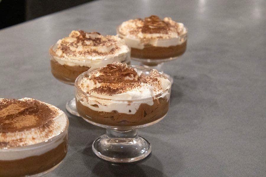 Chilled chocolate mousse desserts in glass cups topped with whipped cream and cocoa powder dusting.