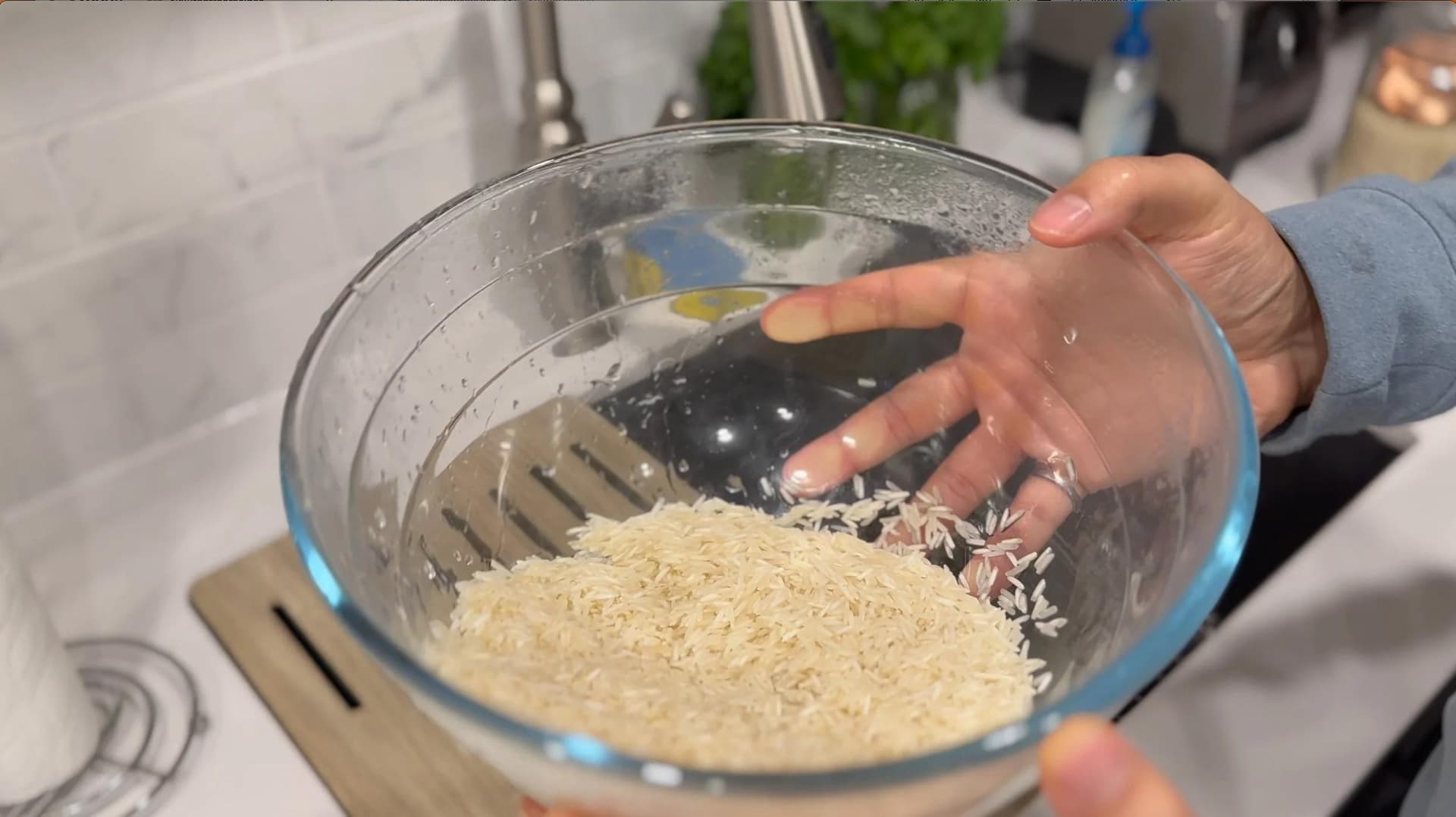 Rinsing rice in a colander held over a glass bowl of water, showing drained rice grains.